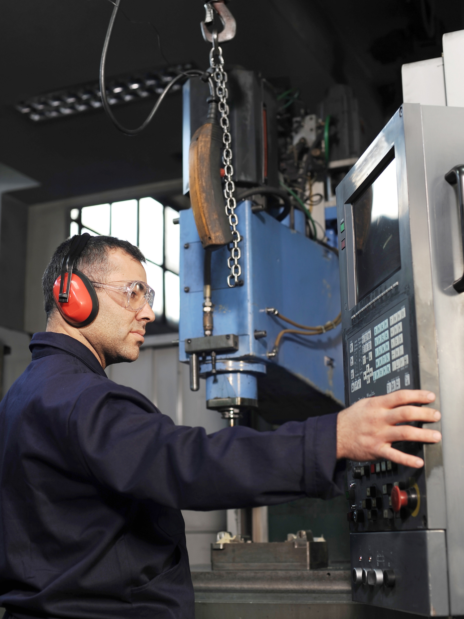 machinist wearing ear protection selecting buttons on a large industrial machine